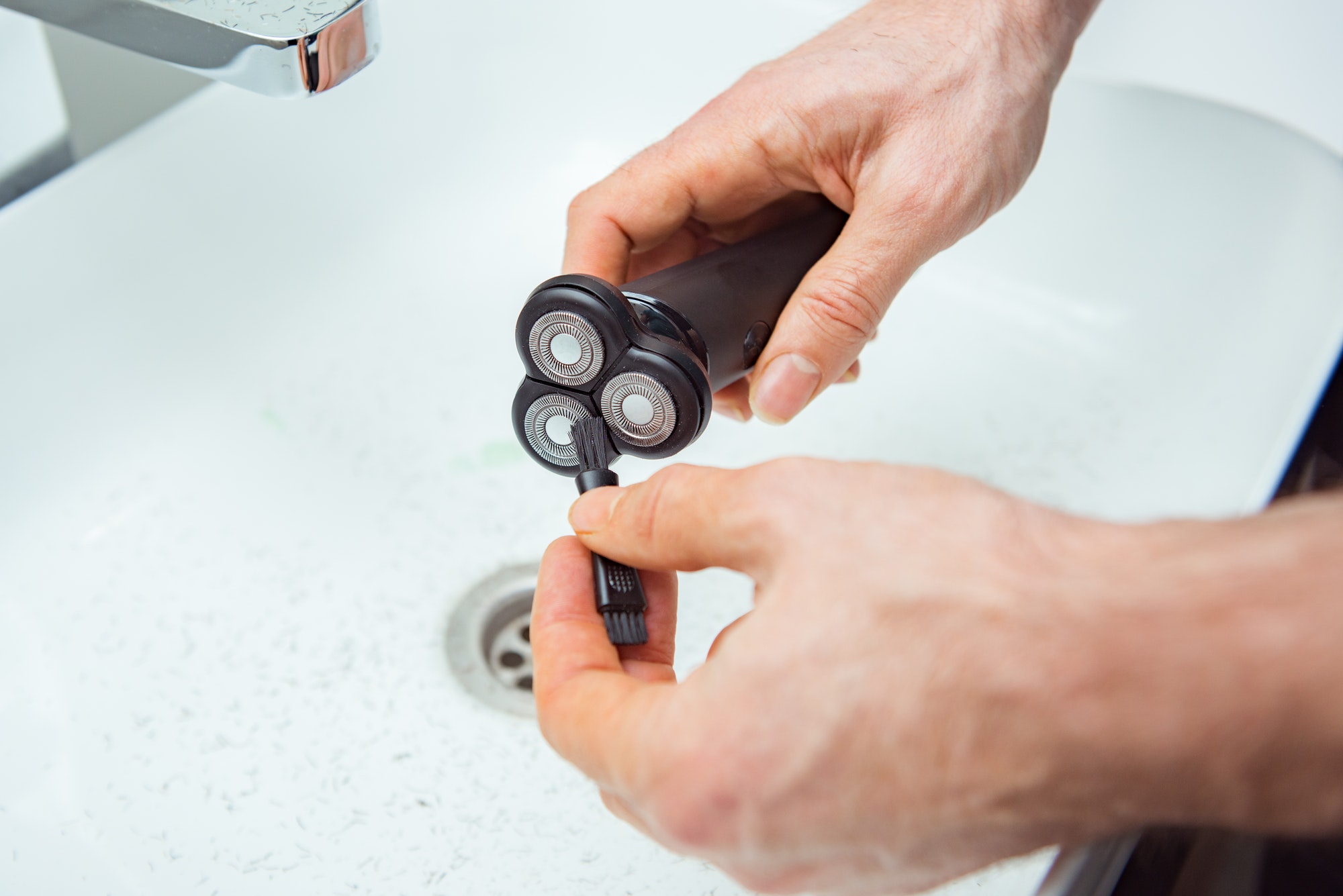 Close up view of a man using the cleaning brush to clean his electric shaver on the wash base