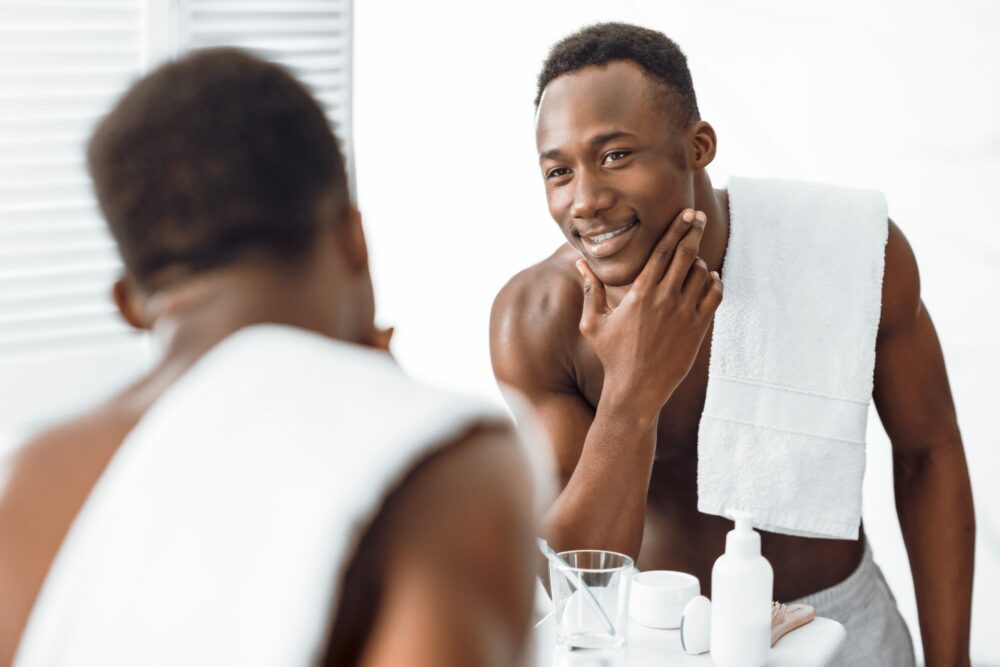 Black Guy Touching Well-Shaved Face Caring For Skin In Bathroom